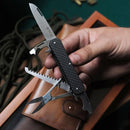 Hand holding a black multitool knife with blade, scissors, saw, and bottle opener opened over a brown leather pouch.