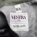Close-up of Vestra 1982 clothing label with size 96M and care instruction symbols inside olive military raincoat