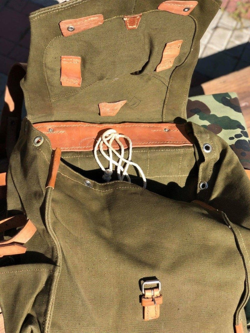 Open genuine Romanian army rucksack made of olive drab canvas with shoulder strap and buckle closure visible