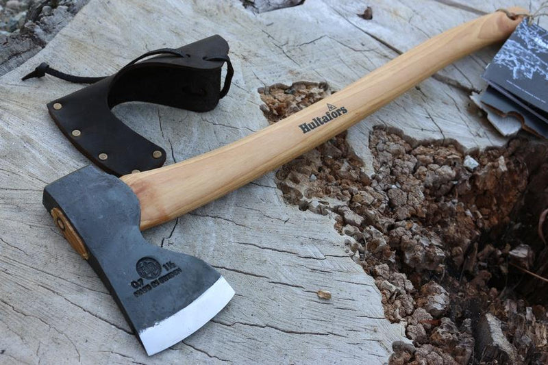 Hultafors ABY Forest Axe with carbon steel head and ergonomic wooden handle resting on a log with blade cover nearby