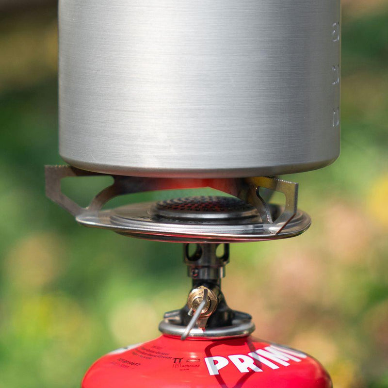 Close-up of a compact Primus Essential Trail Stove burning butane gas with a pot placed on top outdoors.